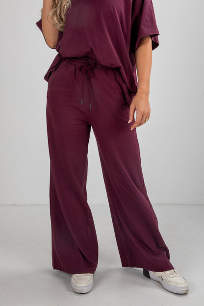 Person wearing a burgundy outfit with wide-leg pants on a white background