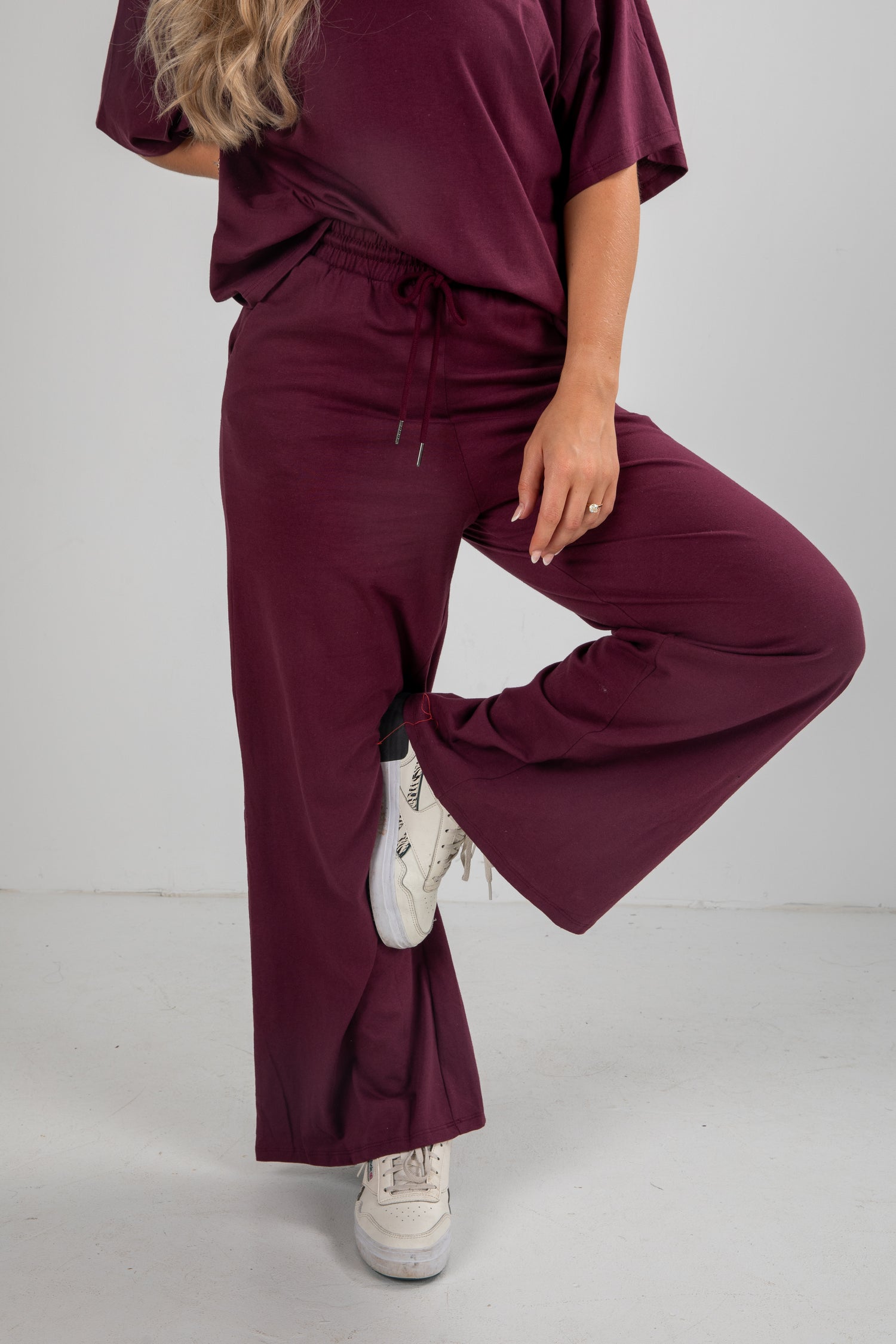 Person wearing a burgundy outfit with white sneakers on a plain background