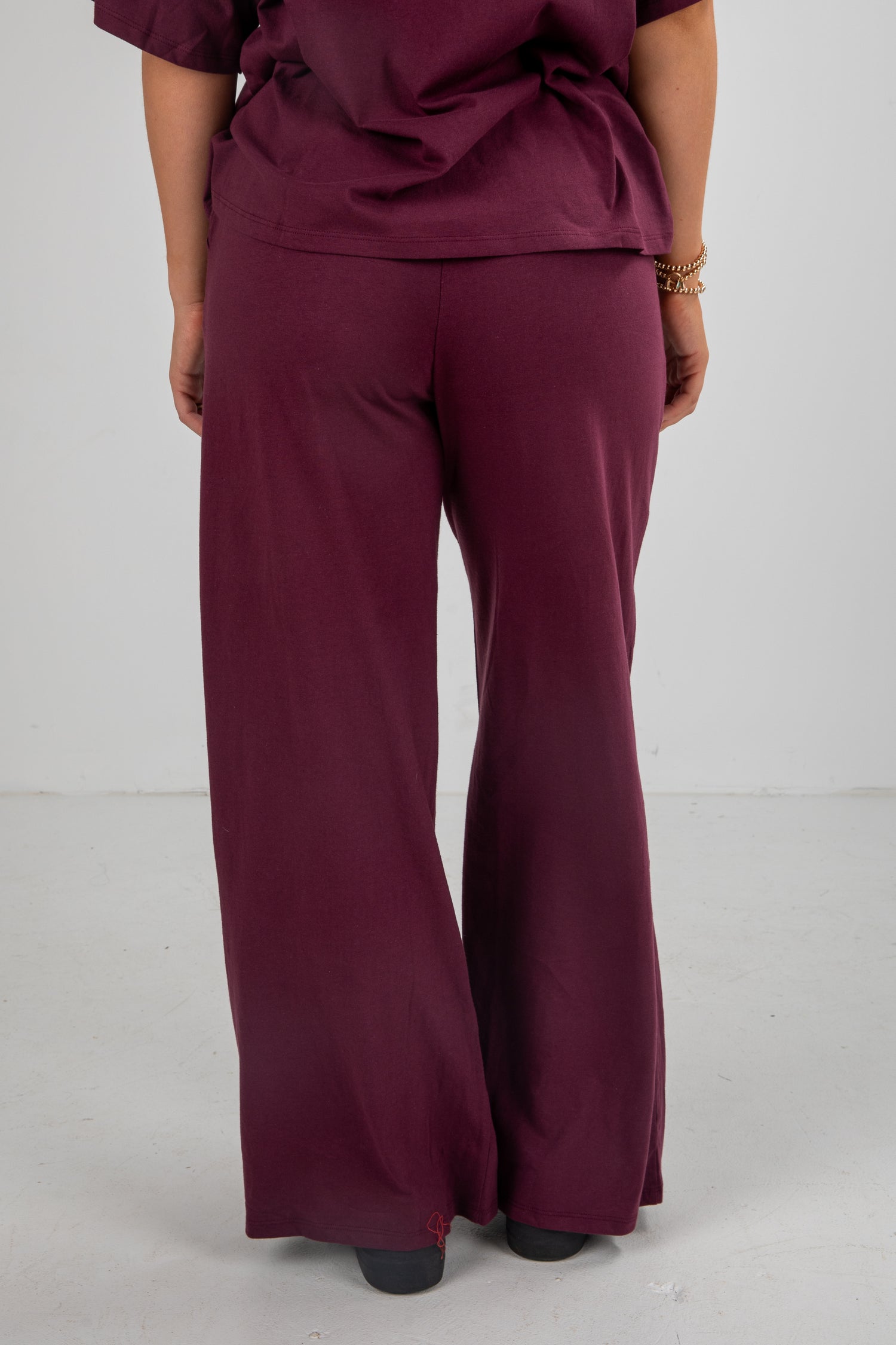 Person wearing a maroon outfit with wide-leg pants on a white background