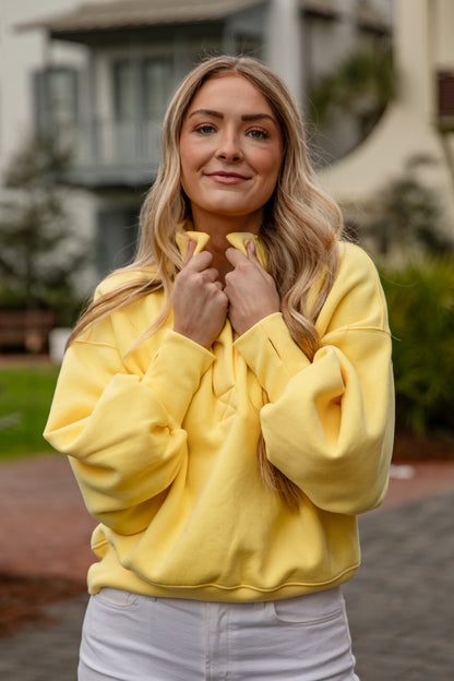 Woman wearing a yellow sweatshirt standing outdoors with a blurred background