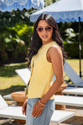 Woman in a yellow top and sunglasses standing in a garden setting with umbrellas.