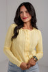 A woman wearing a pale yellow textured knit button-up cardigan sweater and light blue jeans, standing against a light gray wall.