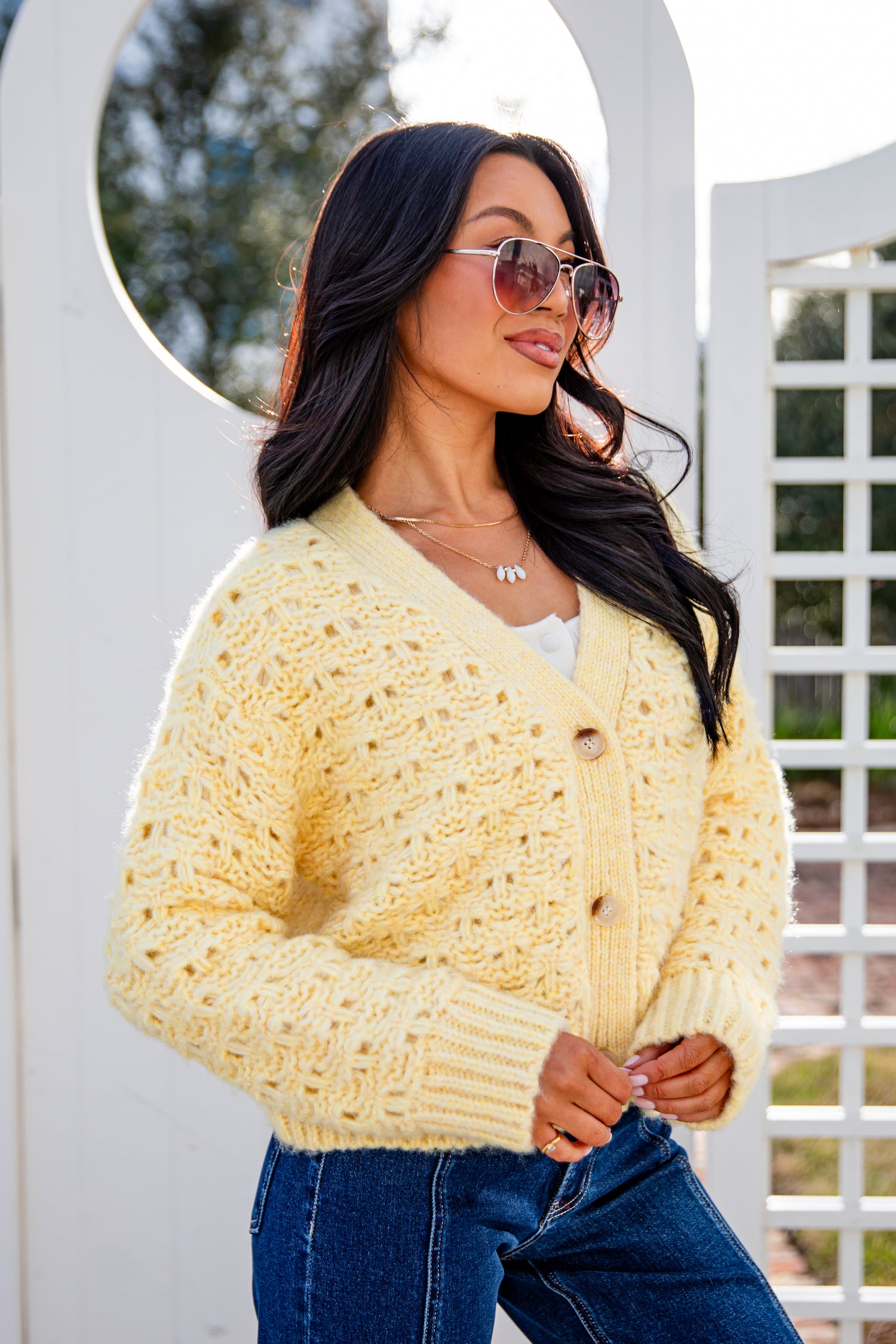 Woman wearing a light yellow cardigan and blue jeans standing outdoors.
