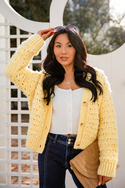 Woman wearing a yellow cardigan, white top, and dark jeans outdoors.