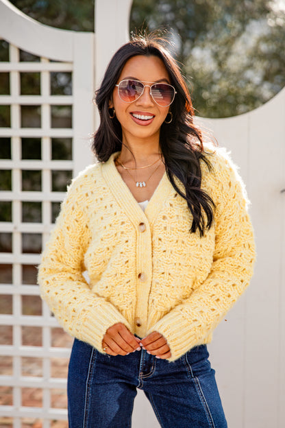 Woman wearing a yellow cardigan and sunglasses outdoors