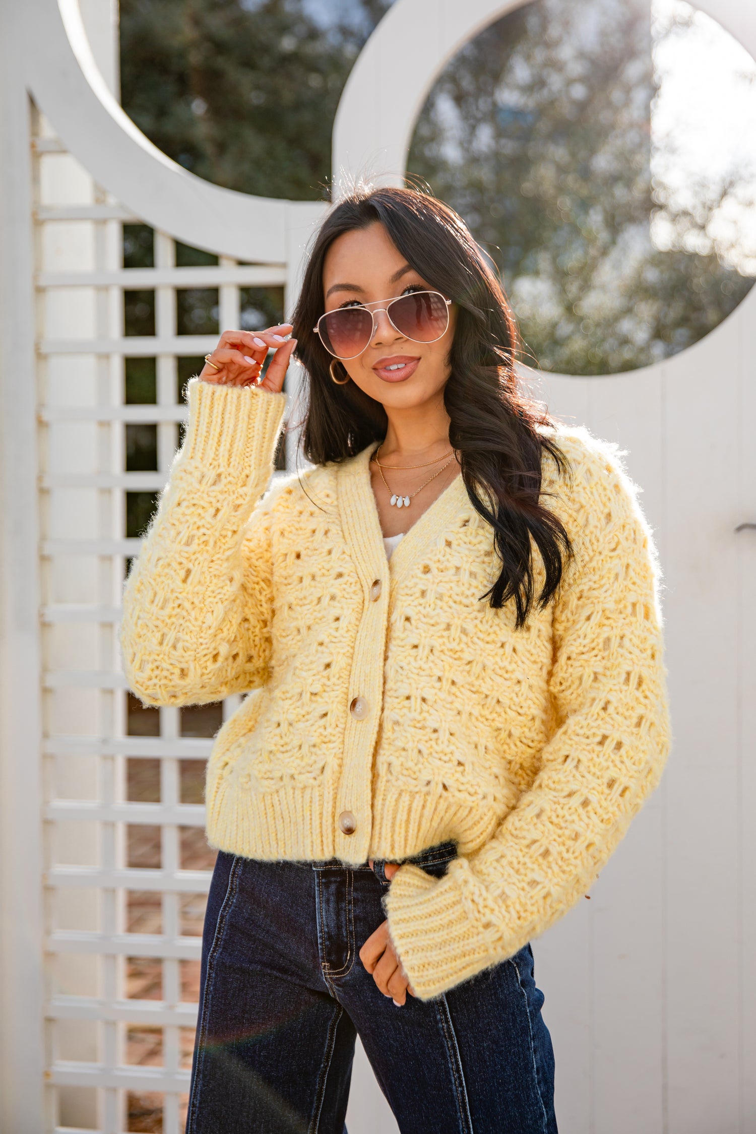 Woman wearing a yellow cardigan and sunglasses outdoors.