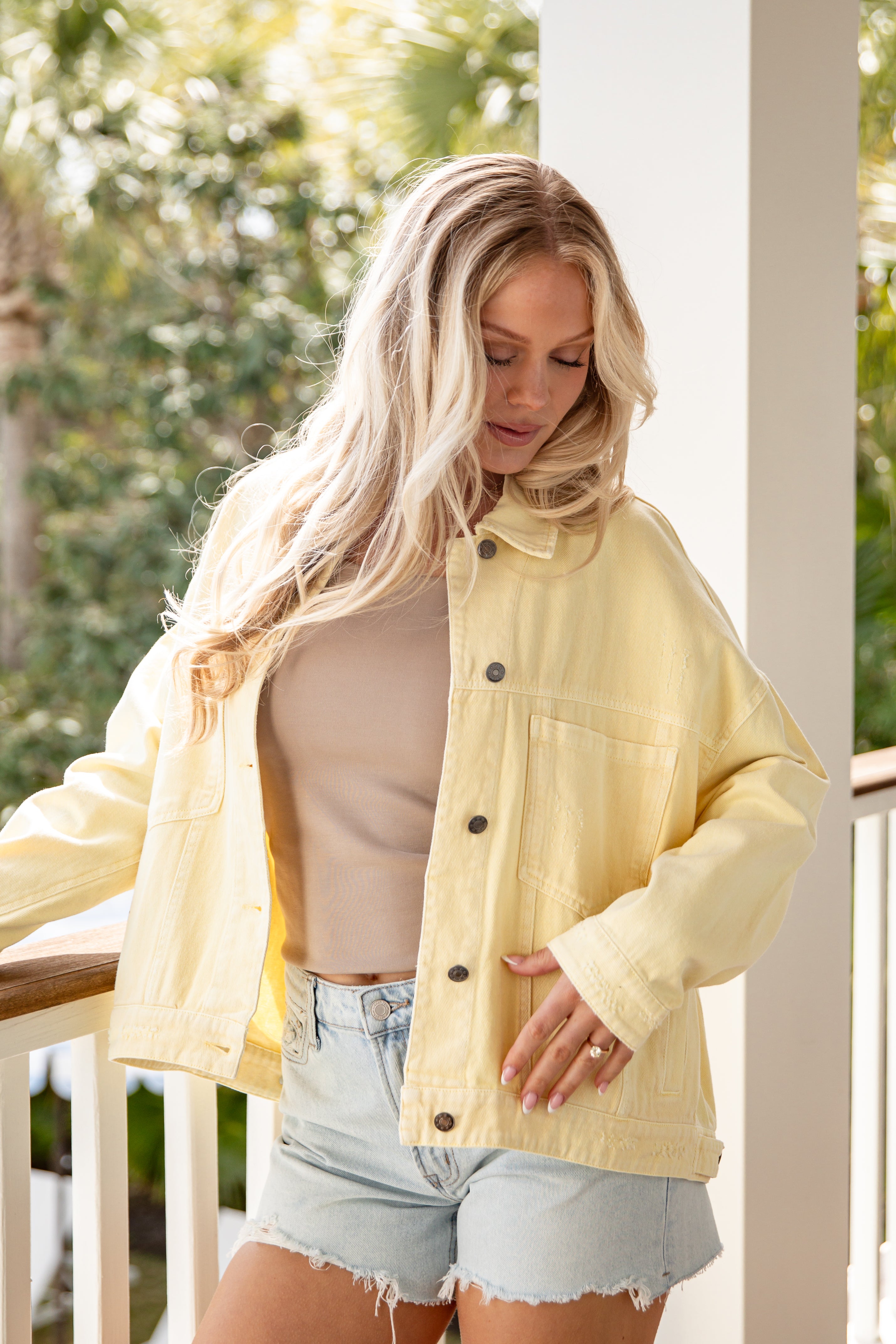 Woman wearing a yellow jacket outdoors with greenery in the background