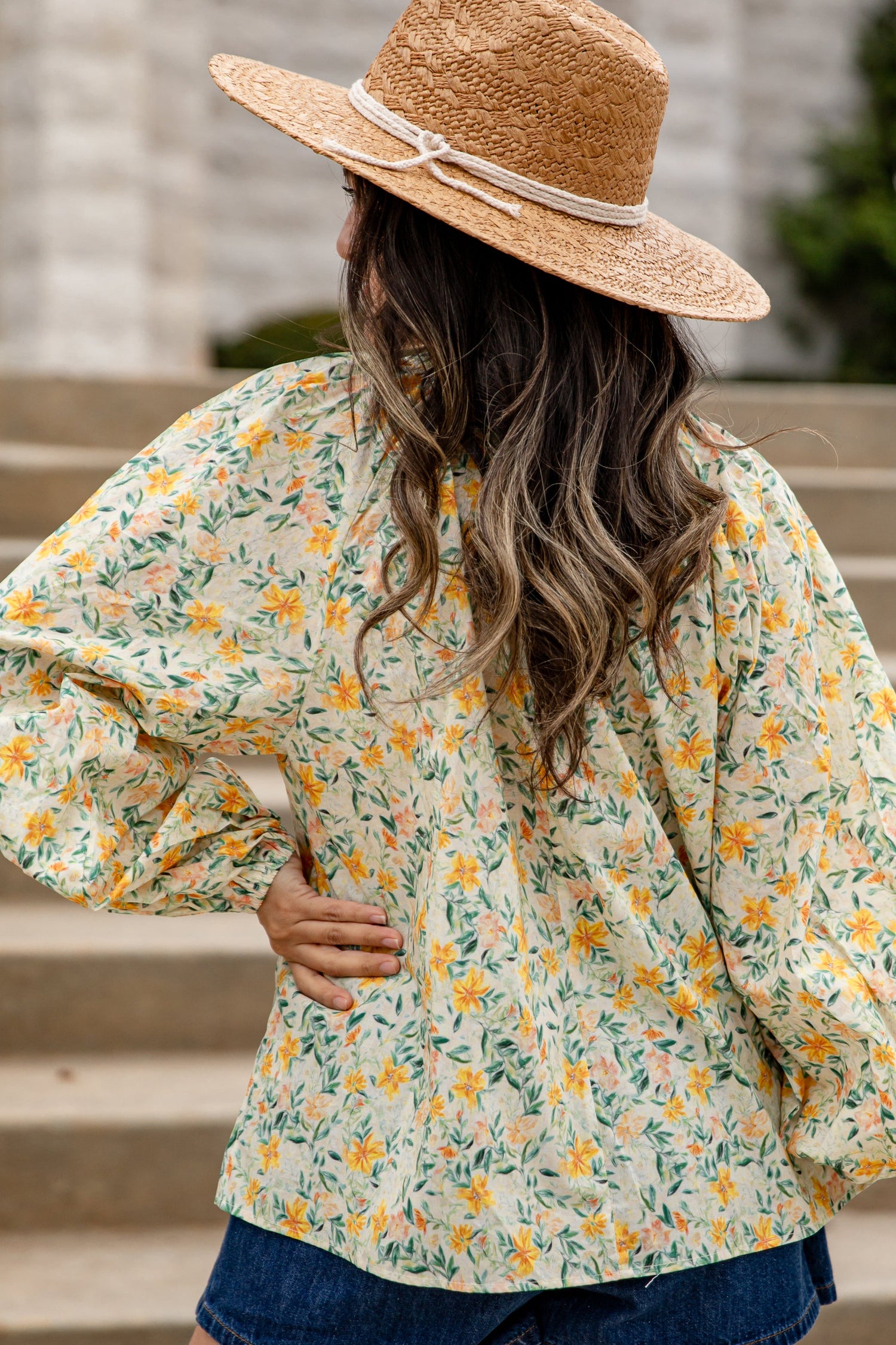 Woman wearing a floral blouse and straw hat standing on steps.