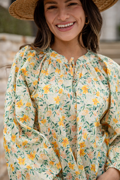 Woman wearing a floral blouse with a straw hat, smiling outdoors.