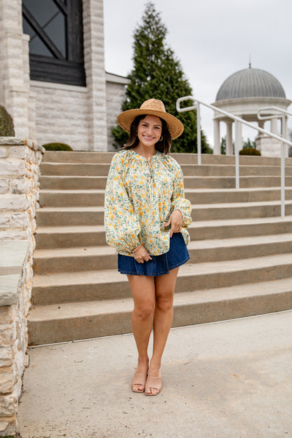 Woman in floral blouse and denim shorts standing on steps outdoors