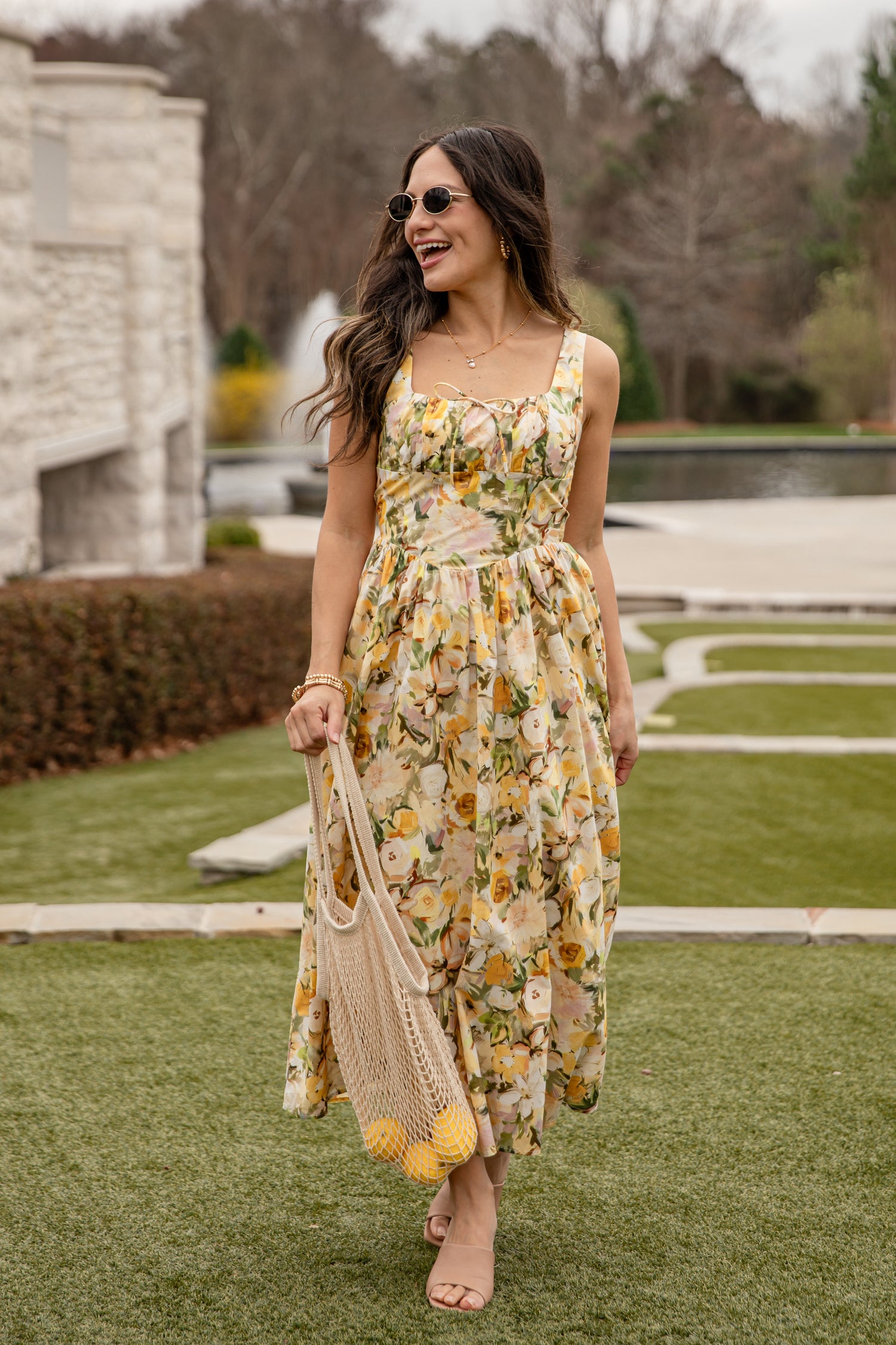 Woman in a floral dress holding a reusable bag on a grassy area.