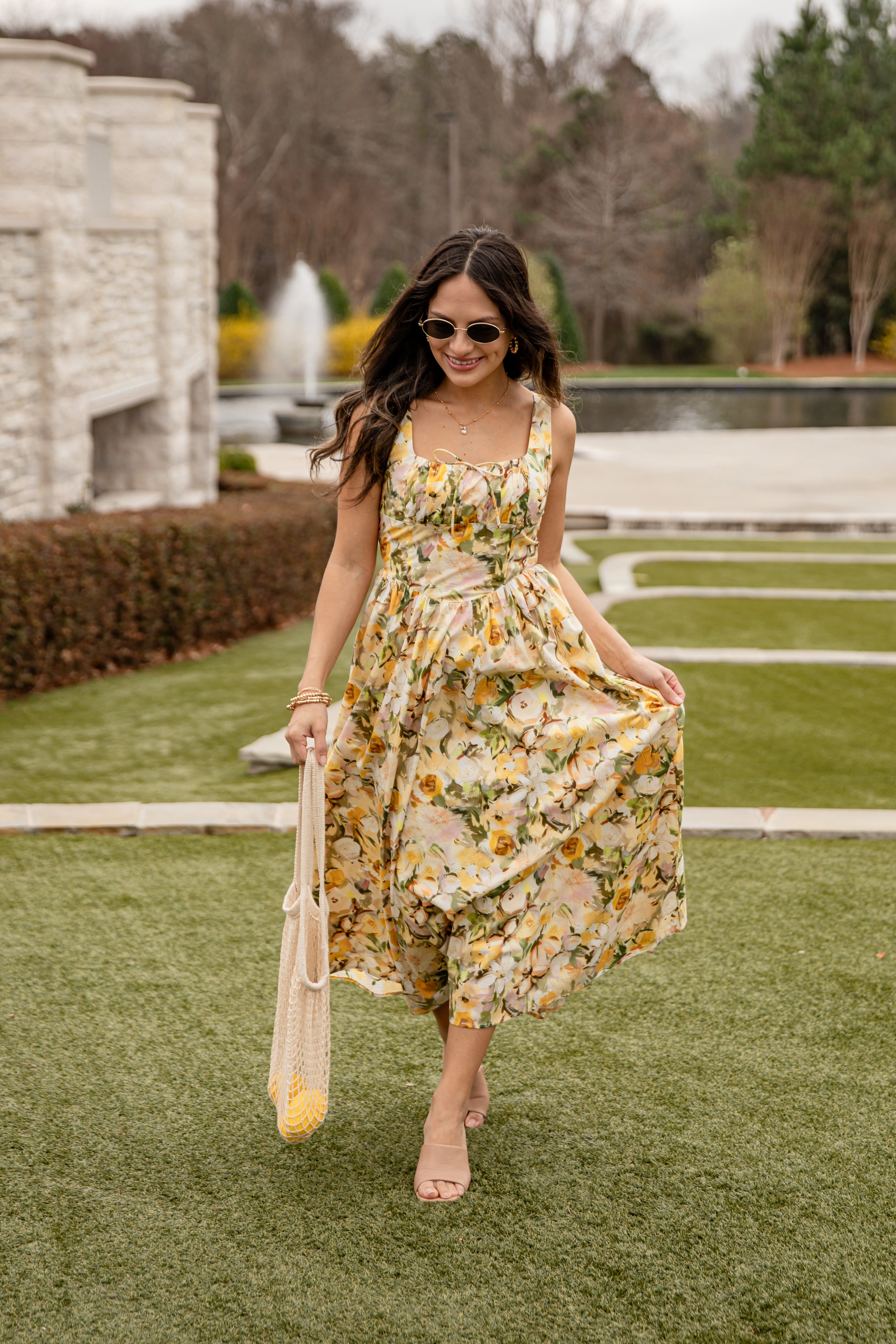 Woman in a floral dress standing on grass with a fountain in the background