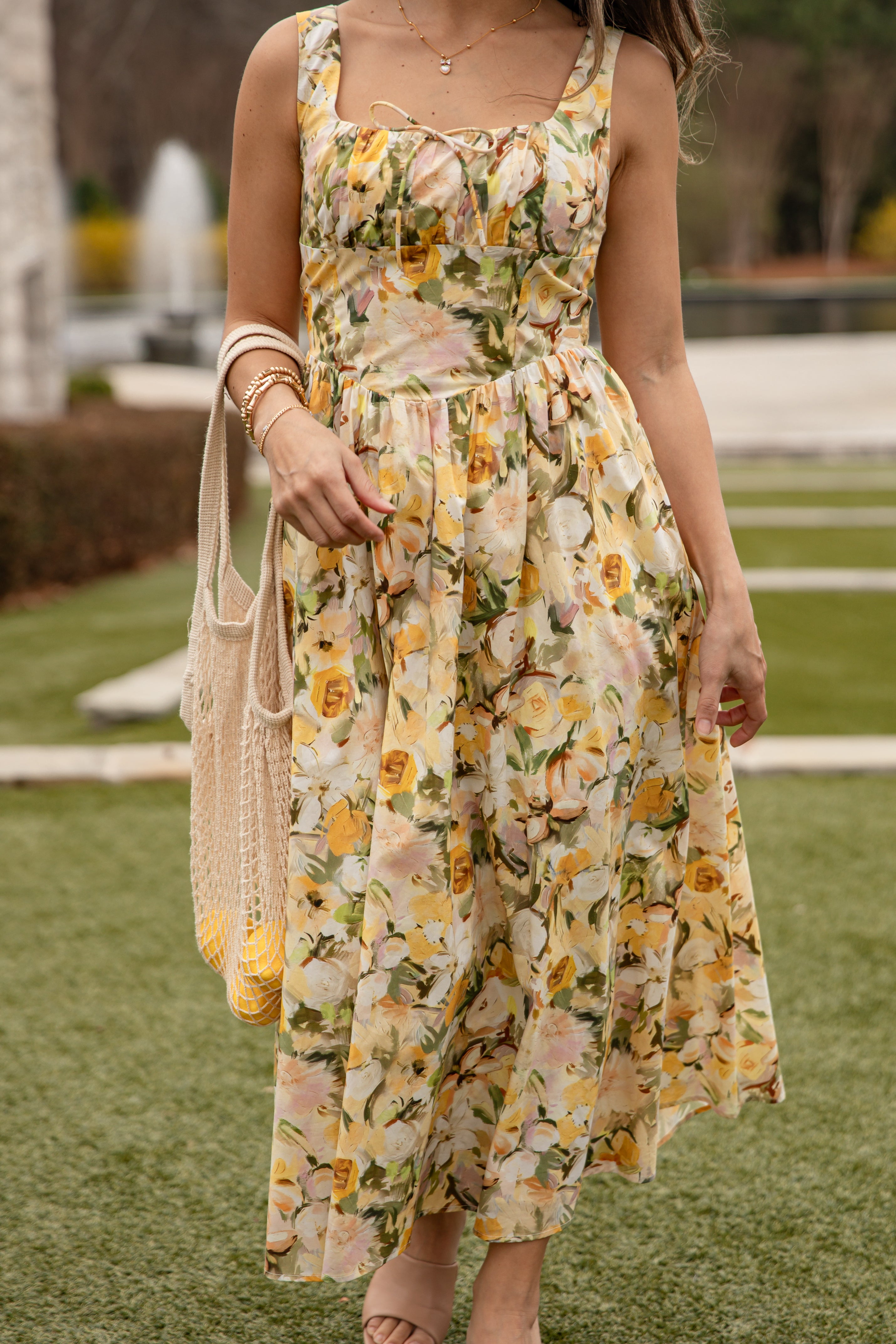 Woman wearing a floral dress with yellow and green flowers, standing on grass.
