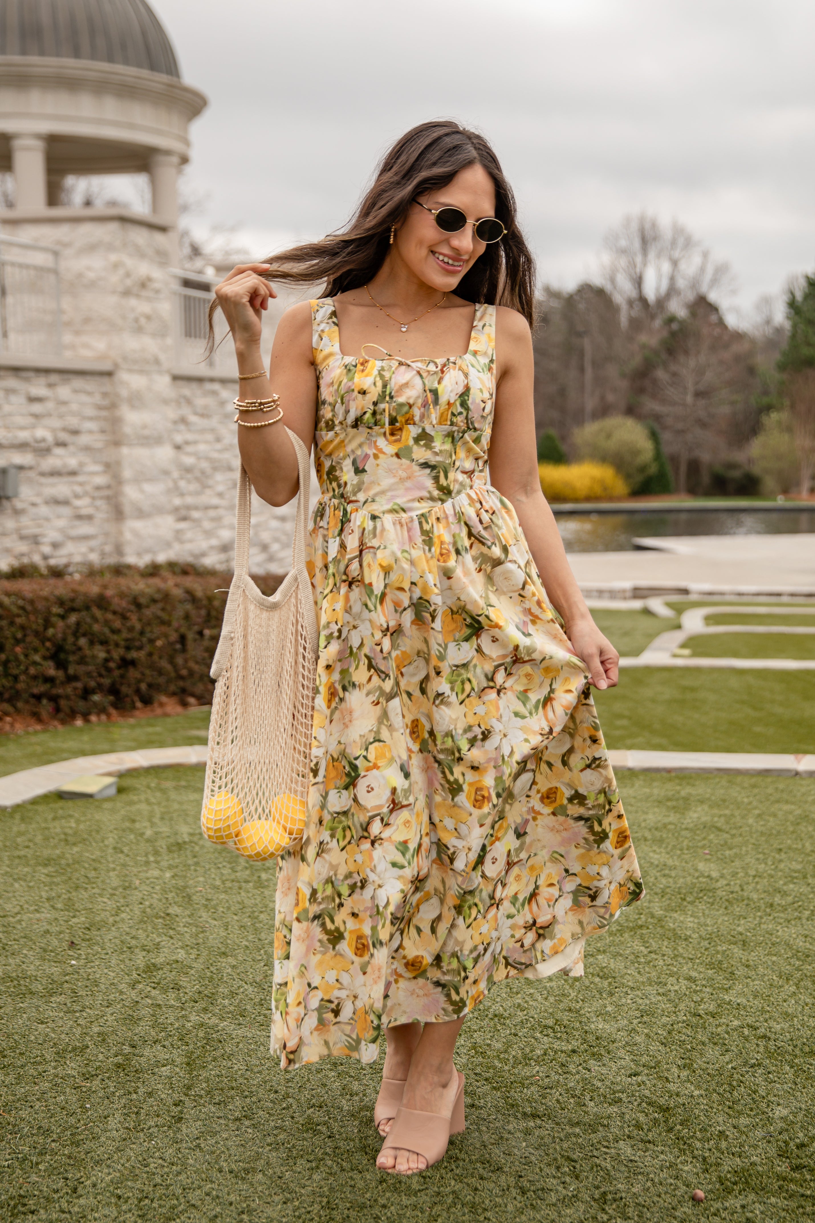 Woman in a floral dress holding a bag with pom-poms, standing outdoors.