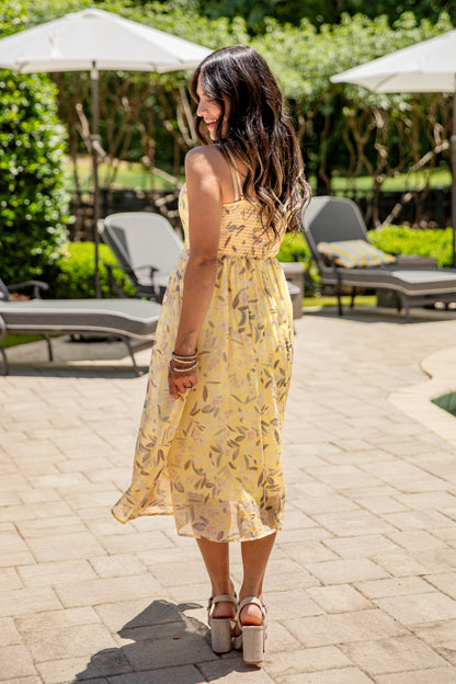 Woman in a yellow dress standing on a patio with lounge chairs and umbrellas in the background.
