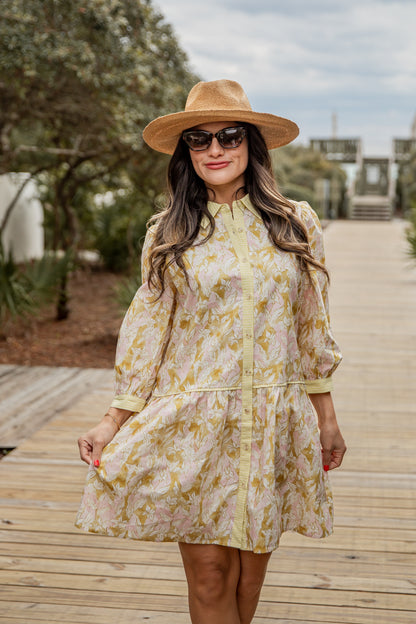 Woman in a floral dress and hat standing on a wooden boardwalk with trees and sky in the background