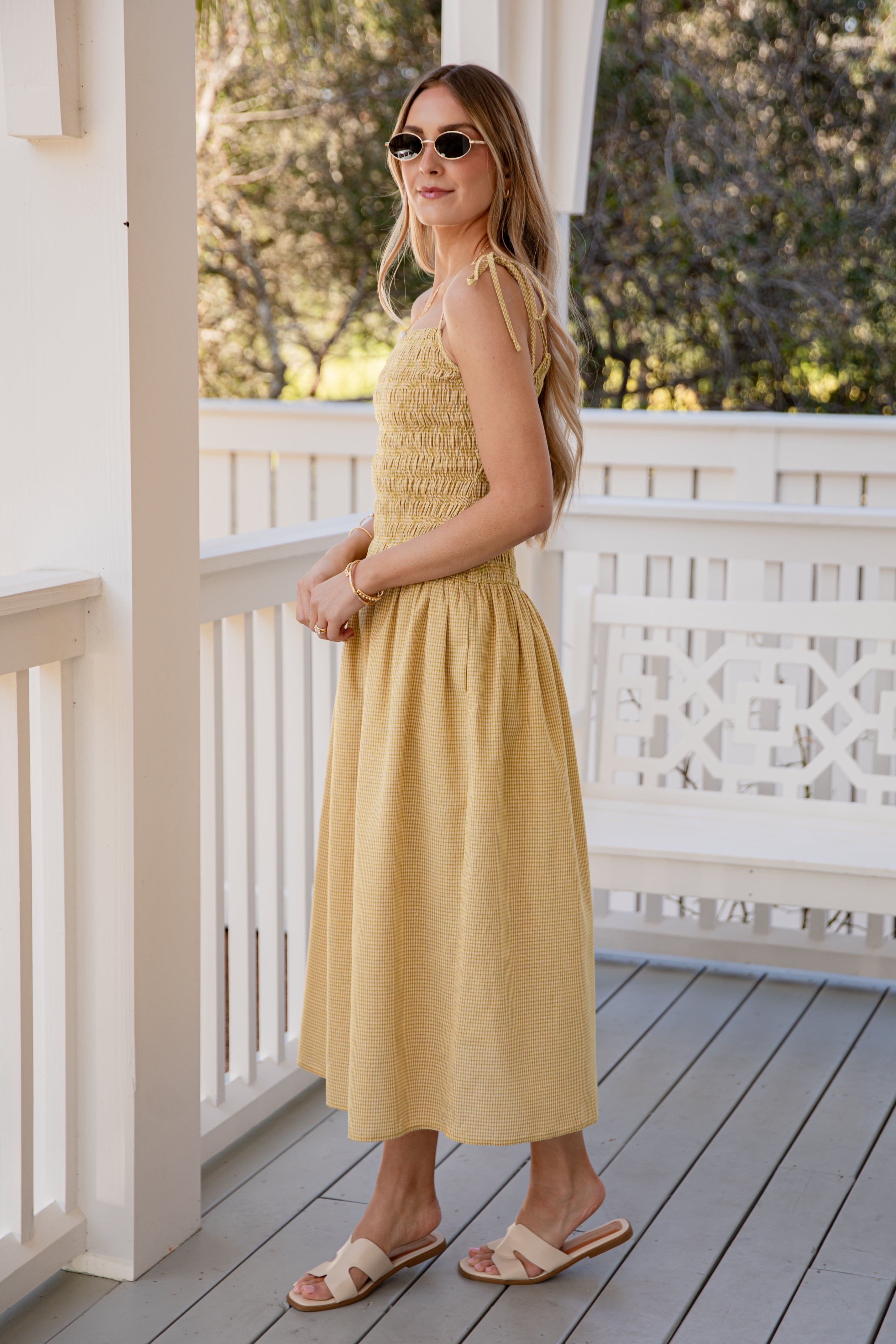 Woman in a yellow dress standing on a wooden deck with white railings.