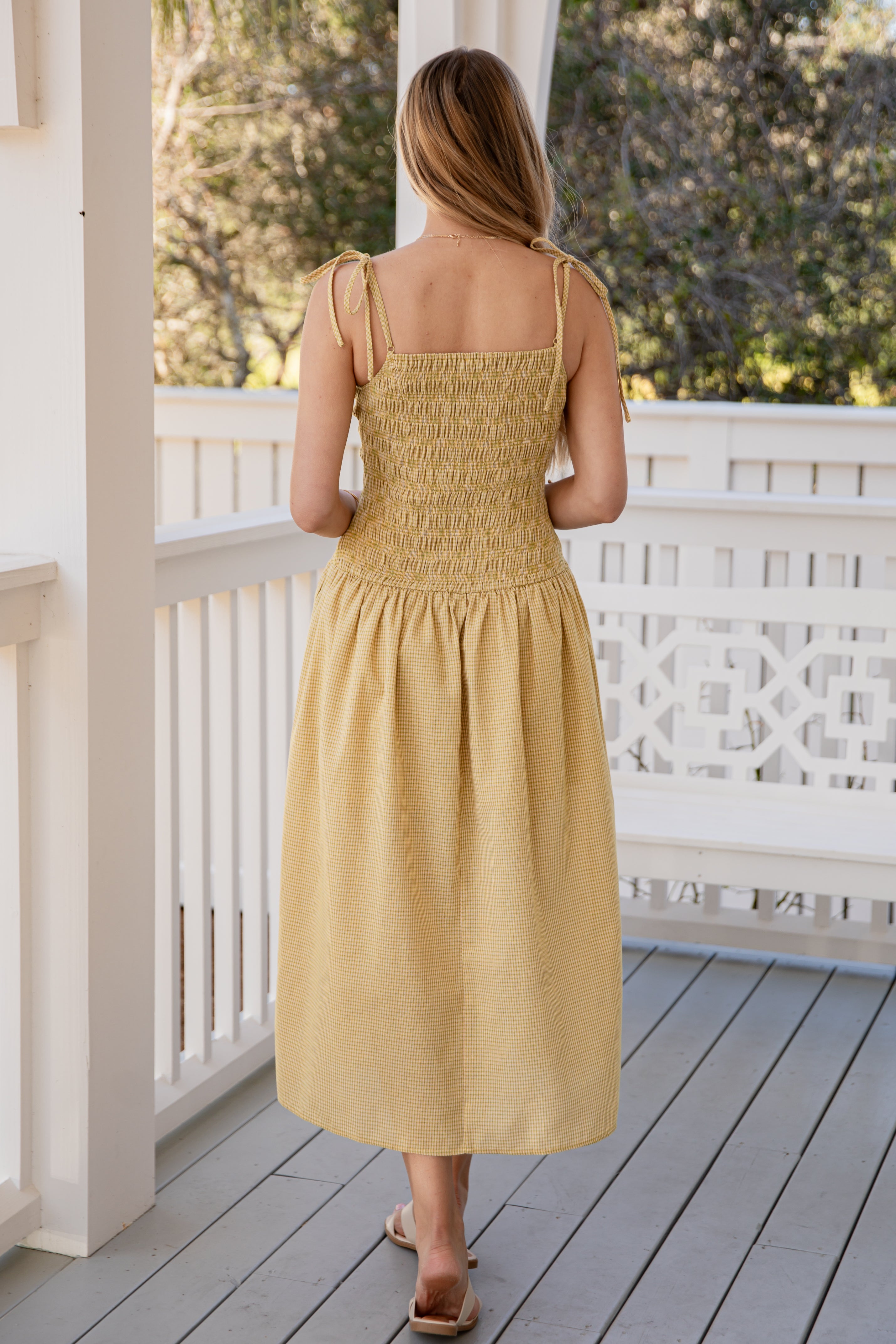 Woman in a yellow dress standing on a wooden deck with a white railing.
