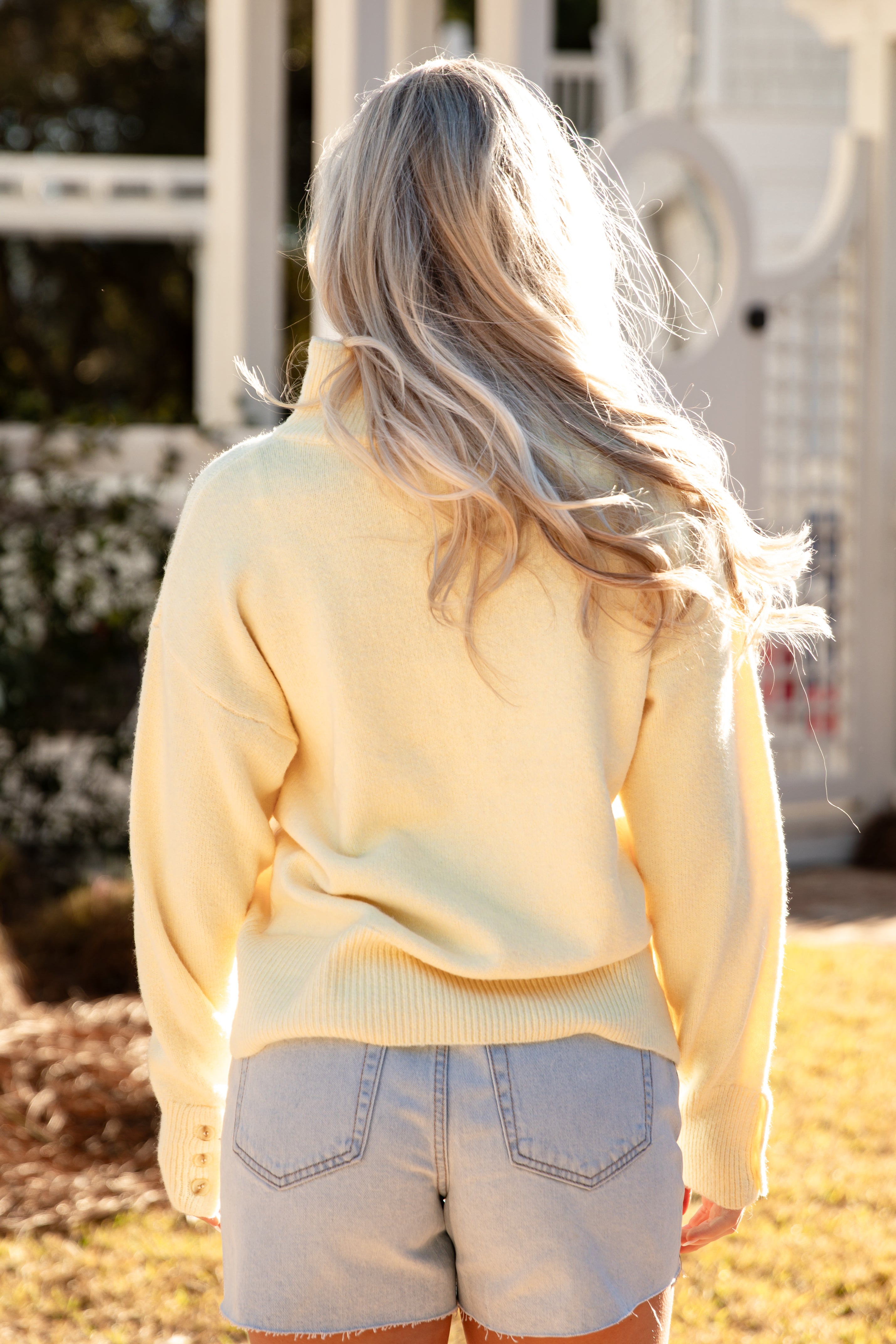 Person wearing a light yellow sweater and denim shorts standing outdoors.