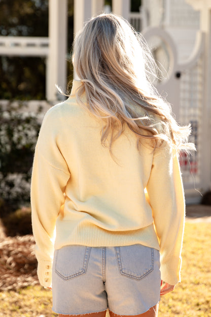 Person wearing a light yellow sweater and denim shorts standing outdoors.