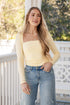 Woman wearing a yellow top and blue jeans standing on a porch.