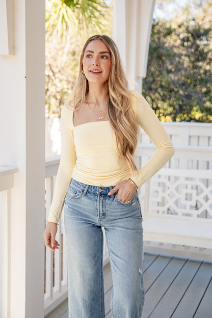 Woman wearing a yellow top and blue jeans standing on a porch.