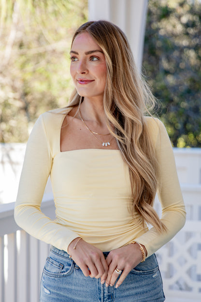 Woman wearing a yellow long-sleeve top and blue jeans on a blurred outdoor background
