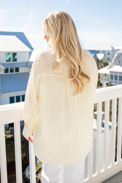 Woman in a light-colored cardigan standing on a balcony with a clear blue sky and buildings in the background