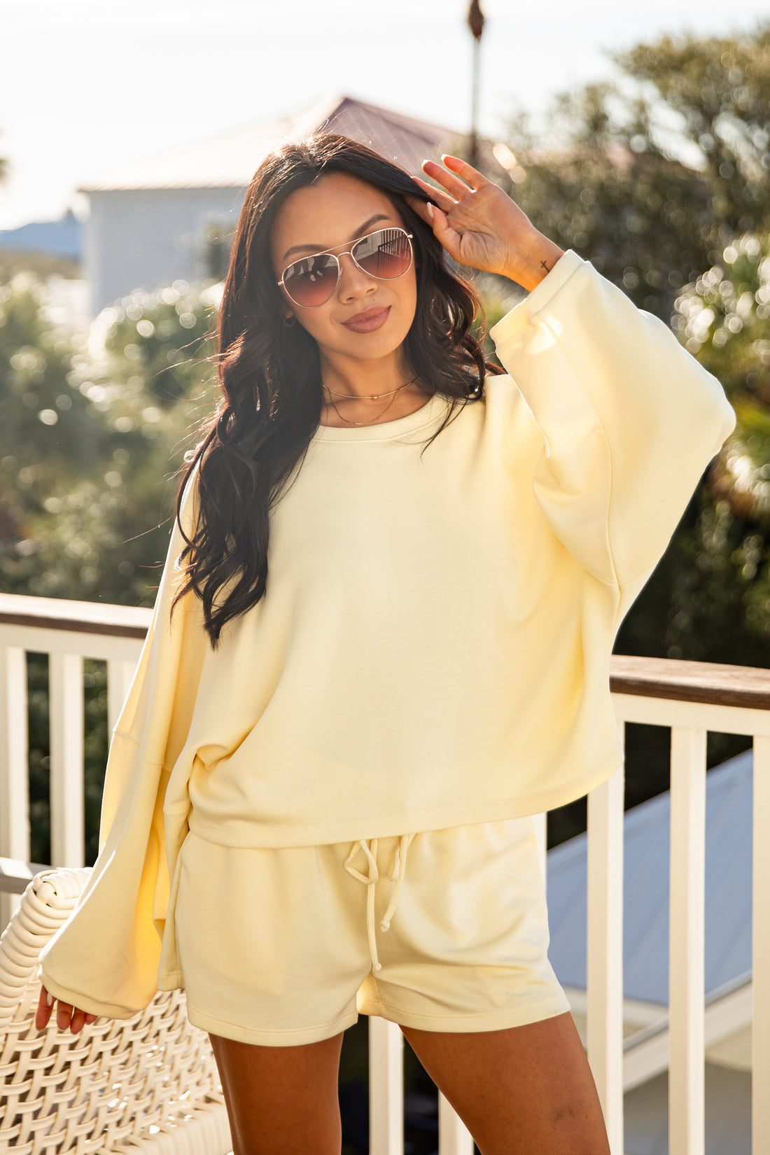 Woman in a light yellow outfit standing on a balcony with greenery in the background