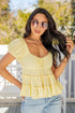 Woman wearing a yellow ruffled top and sunglasses outdoors