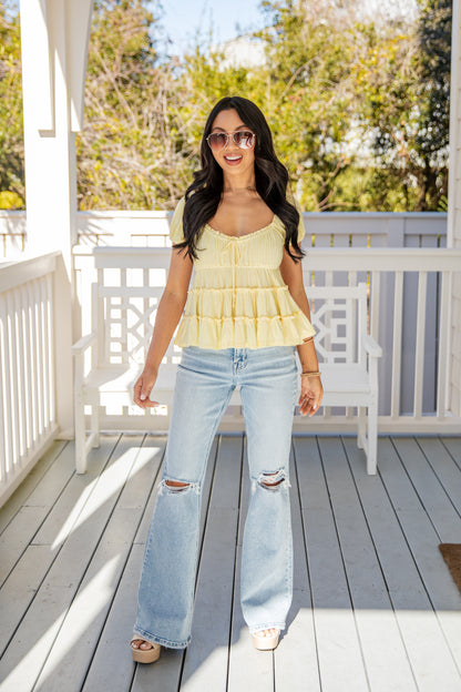 Woman wearing a yellow top and light blue jeans on a wooden deck.