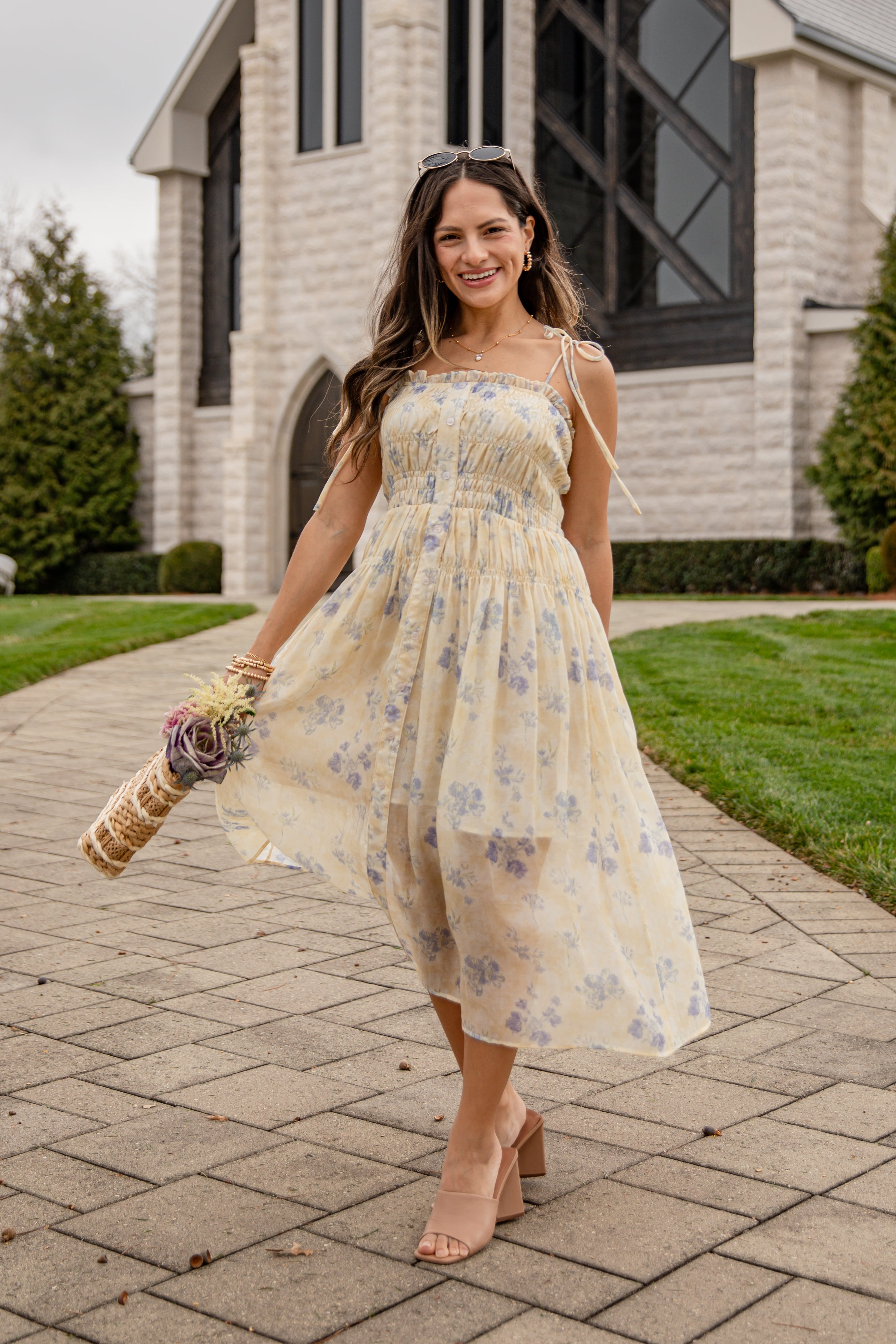 Woman in a floral dress standing on a brick pathway with a house in the background