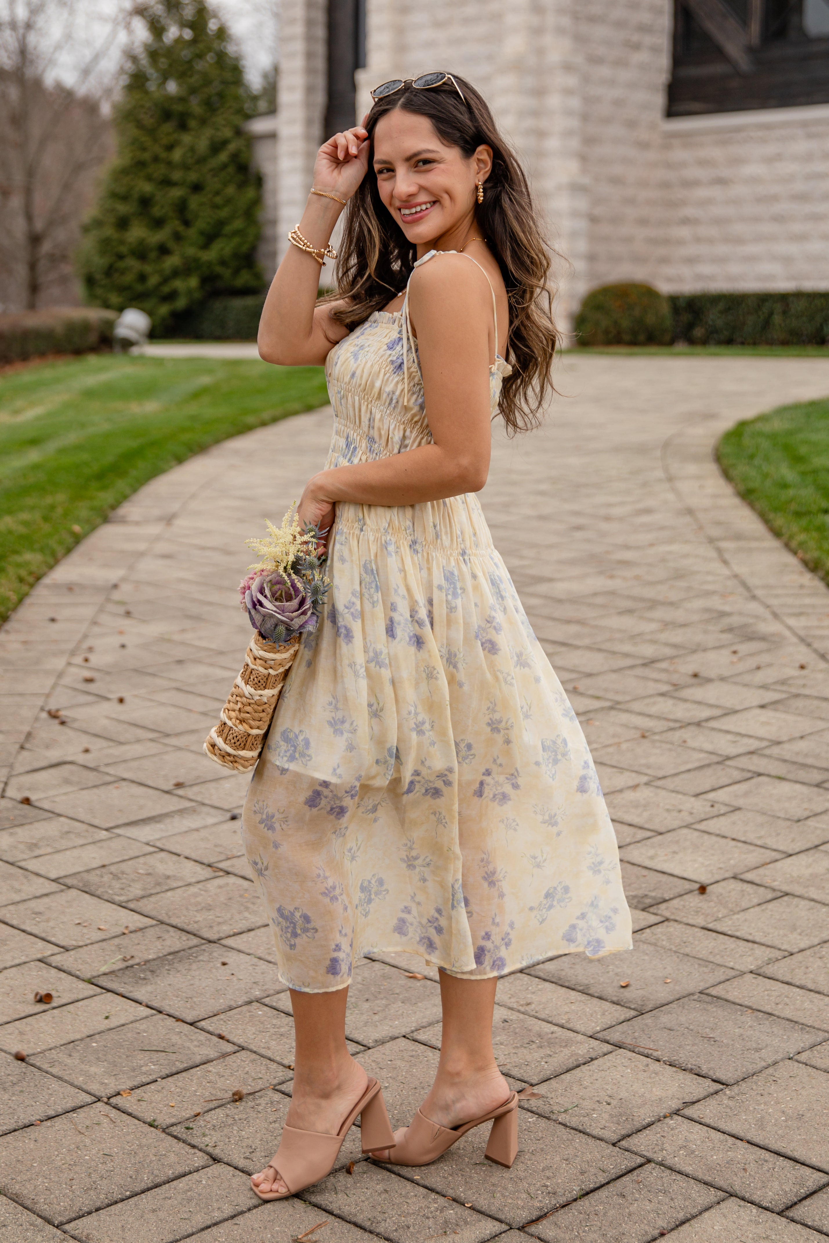 Woman in a floral dress holding a bouquet on a paved walkway.