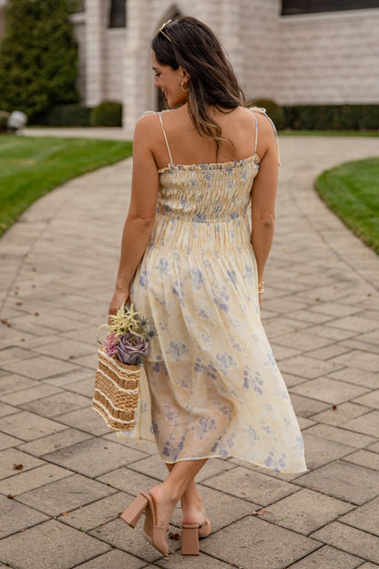 Woman in a floral dress walking on a paved path with a house in the background