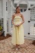 Woman in a yellow strapless dress standing on a brick patio.