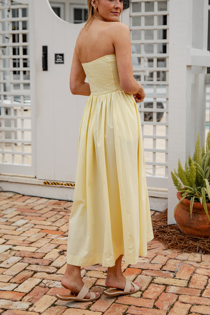 Woman in a yellow strapless dress standing on a brick patio.