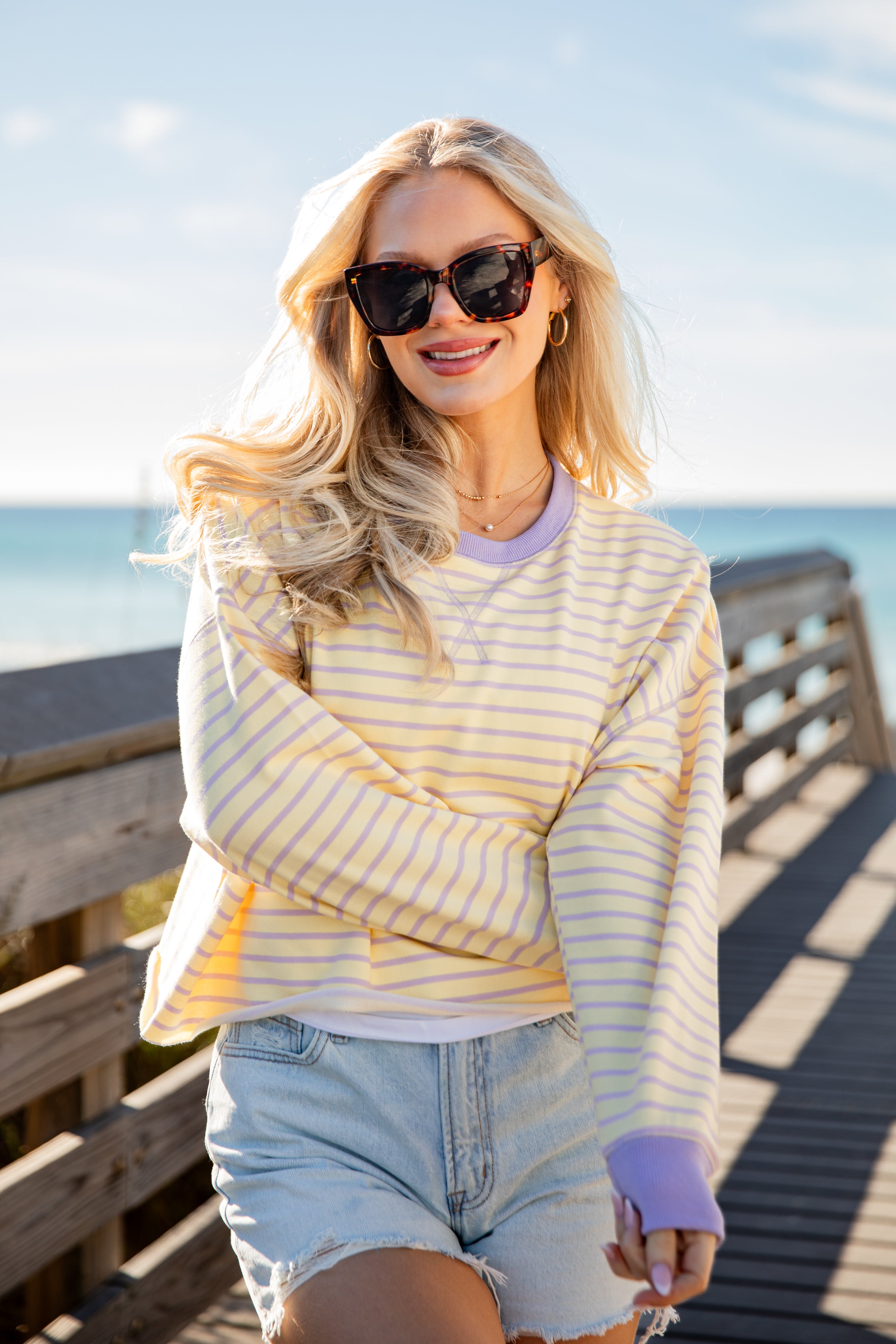 Woman wearing a striped shirt and sunglasses on a wooden pier with ocean view