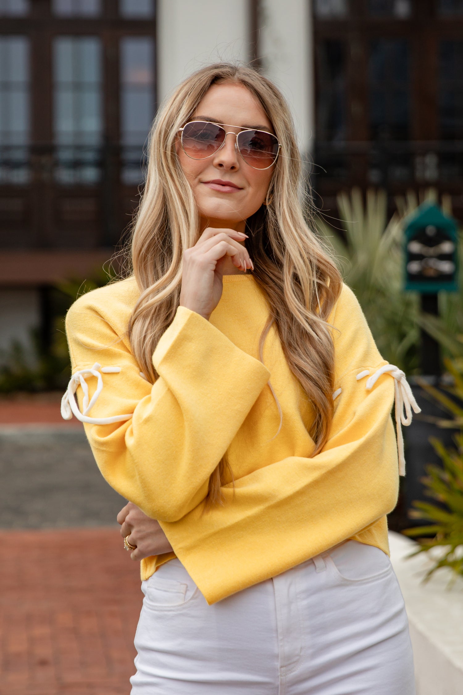 Woman wearing a yellow sweater with white tassel details outdoors.