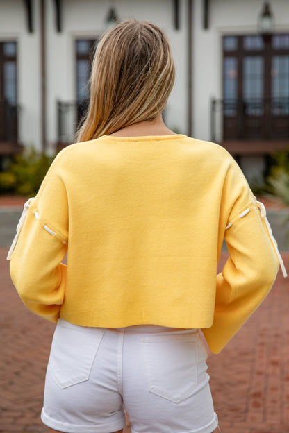 Person wearing a yellow sweater with white accents in front of a building.