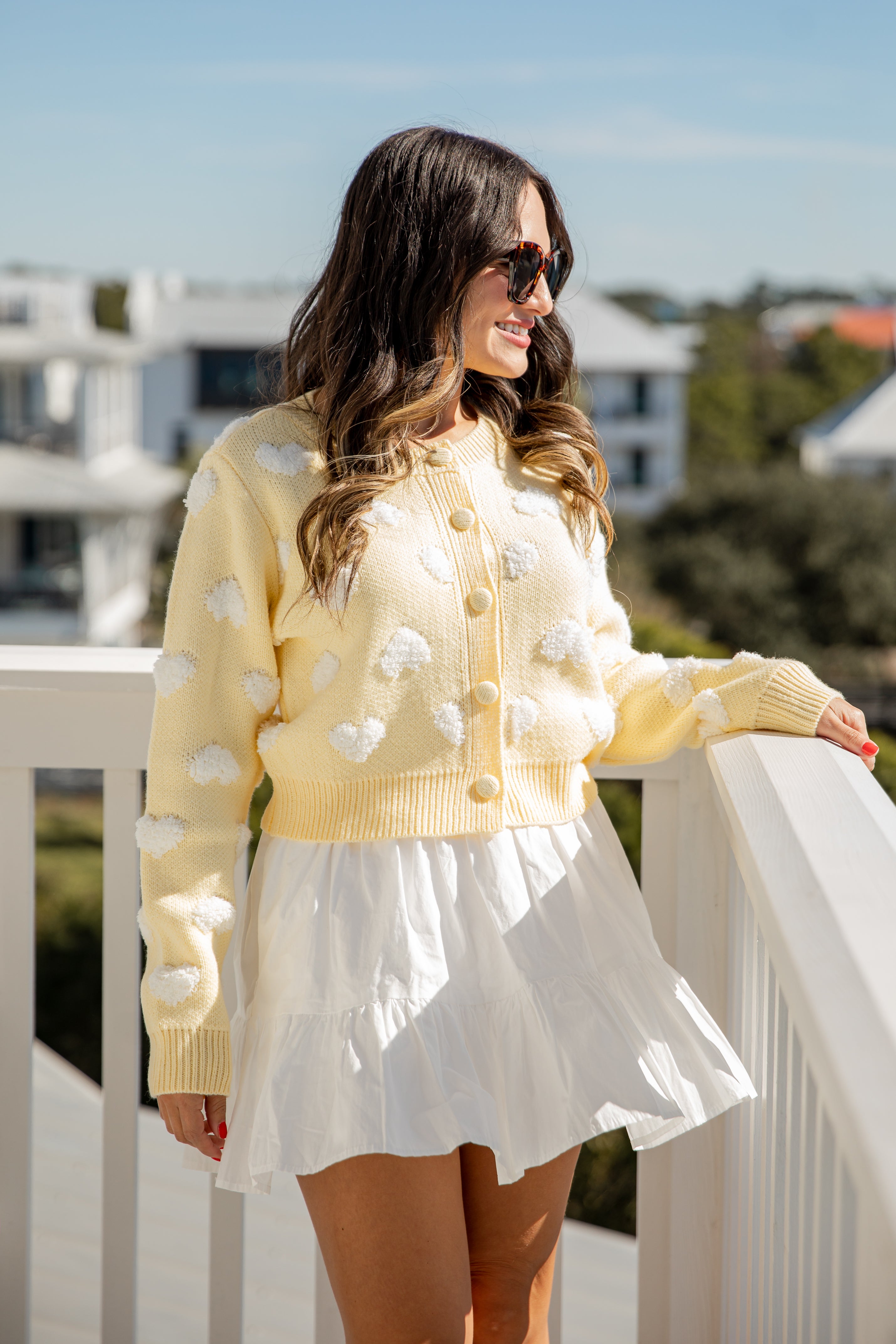 Woman wearing a yellow polka dot cardigan and white dress on a balcony.