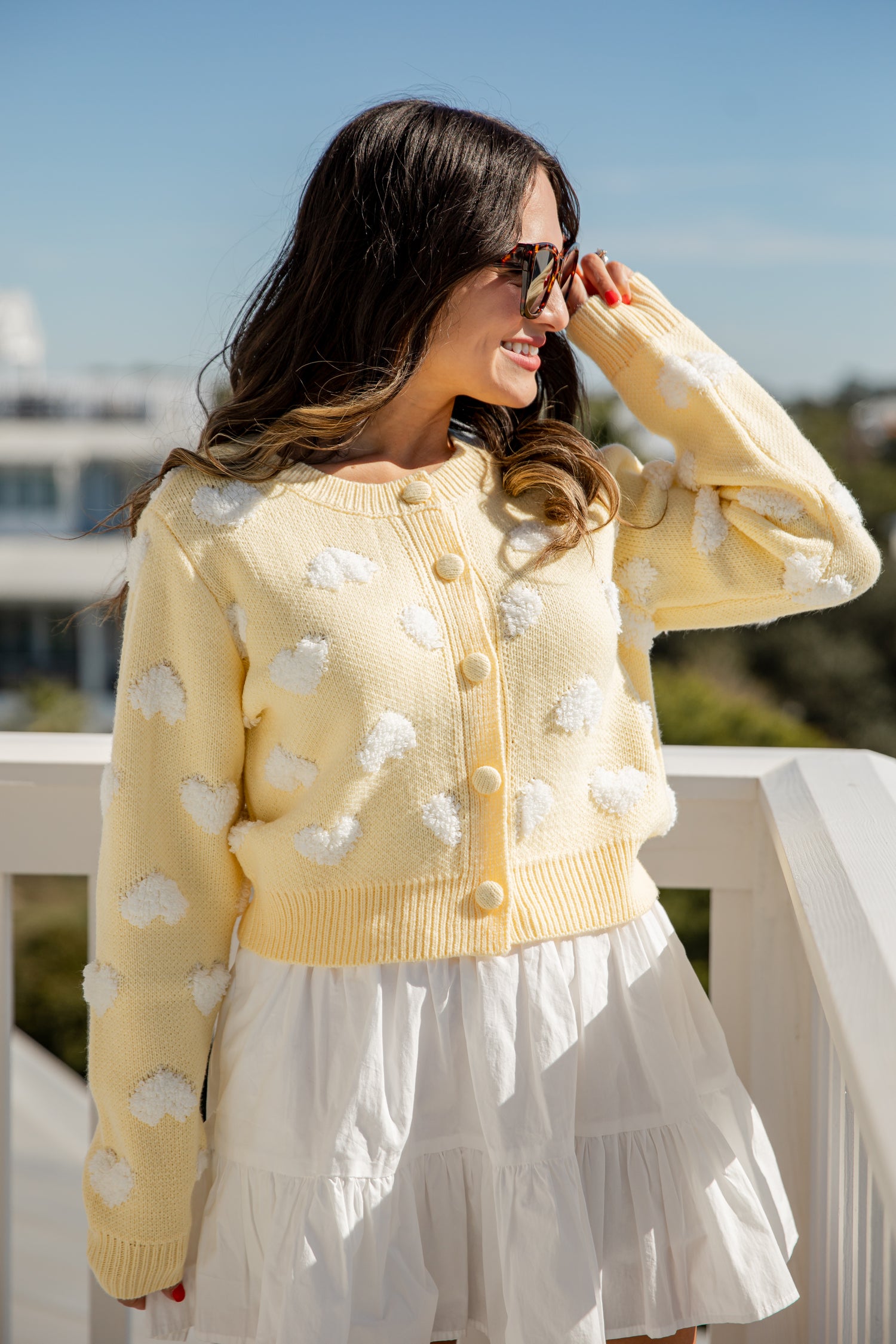 Woman wearing a yellow cardigan with white cloud patterns on a balcony.