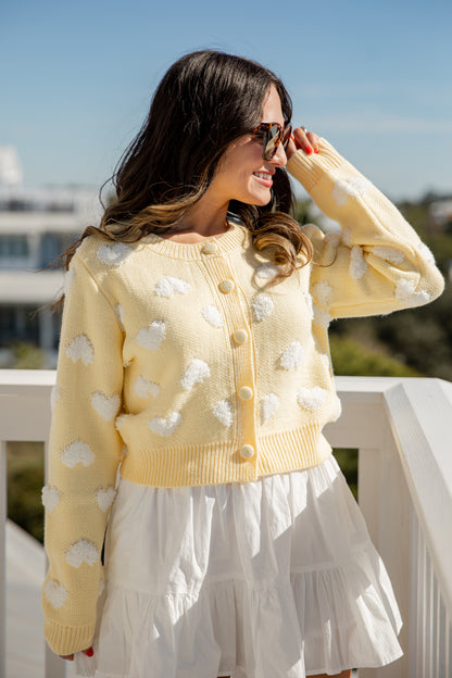 Woman wearing a yellow cardigan with white cloud patterns on a balcony.