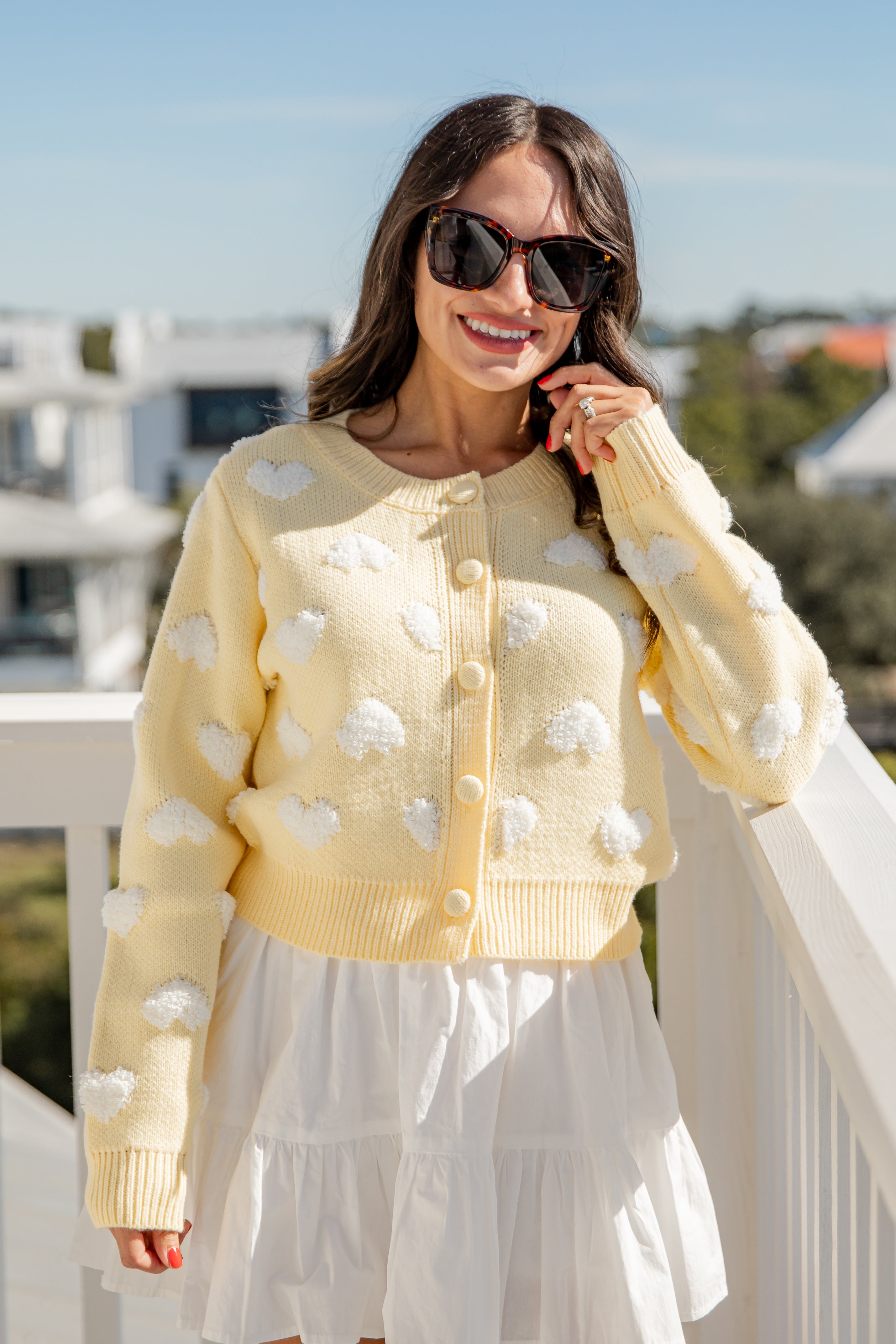 Woman wearing a yellow cardigan with white polka dots and sunglasses, standing outdoors.