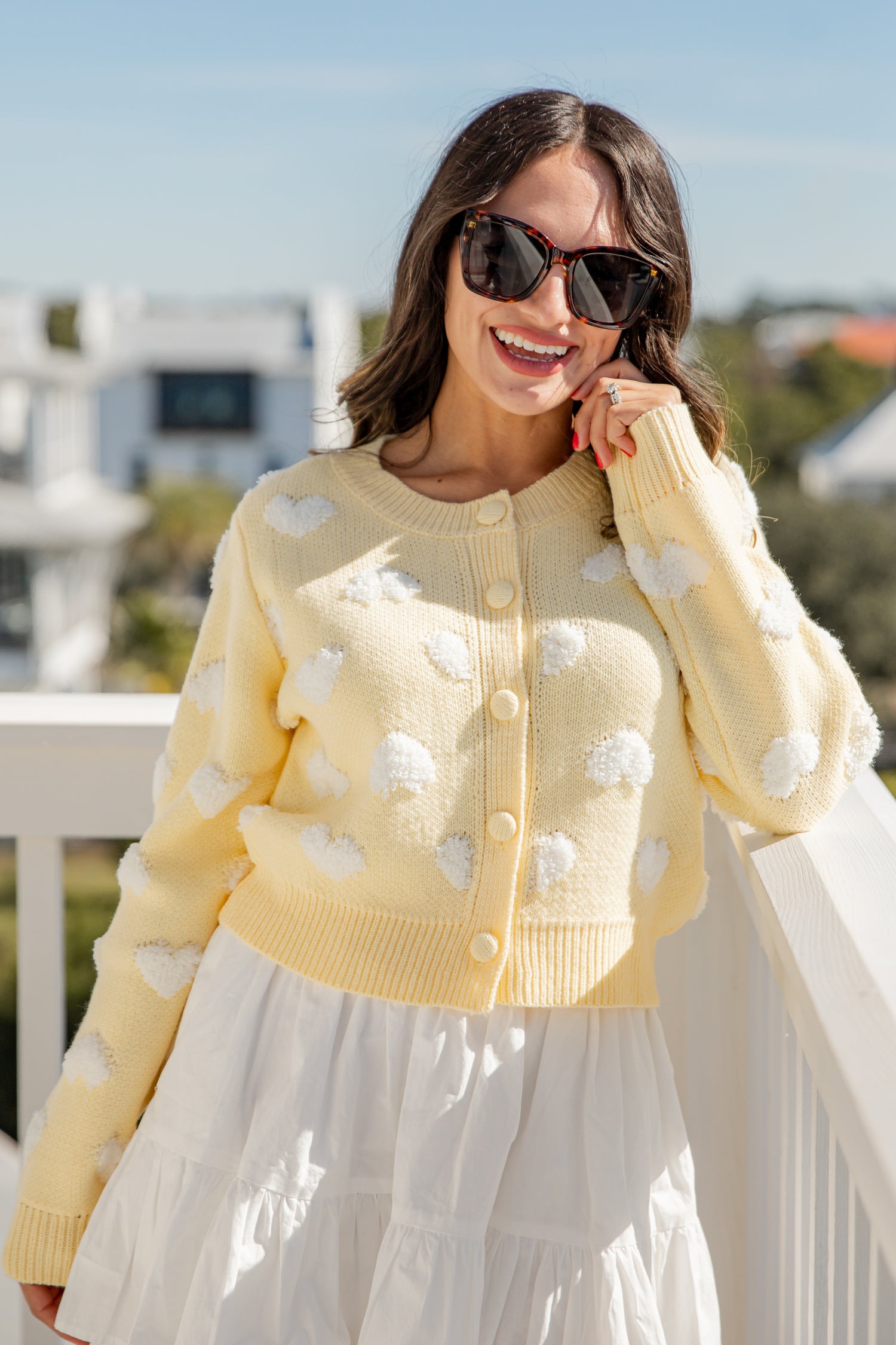Woman wearing a yellow cardigan with white cloud patterns outdoors.