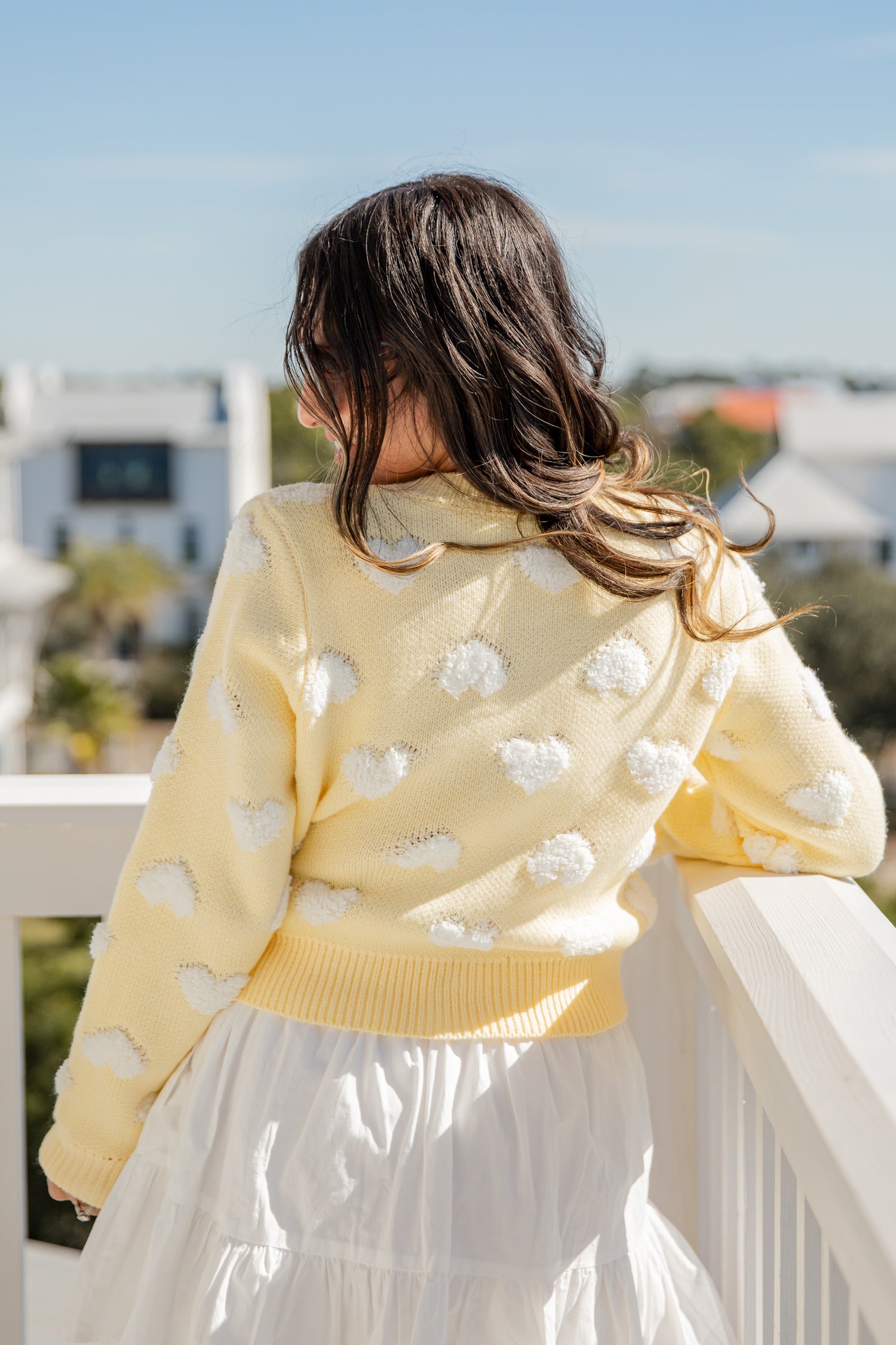 Person wearing a yellow sweater with white cloud patterns on a balcony