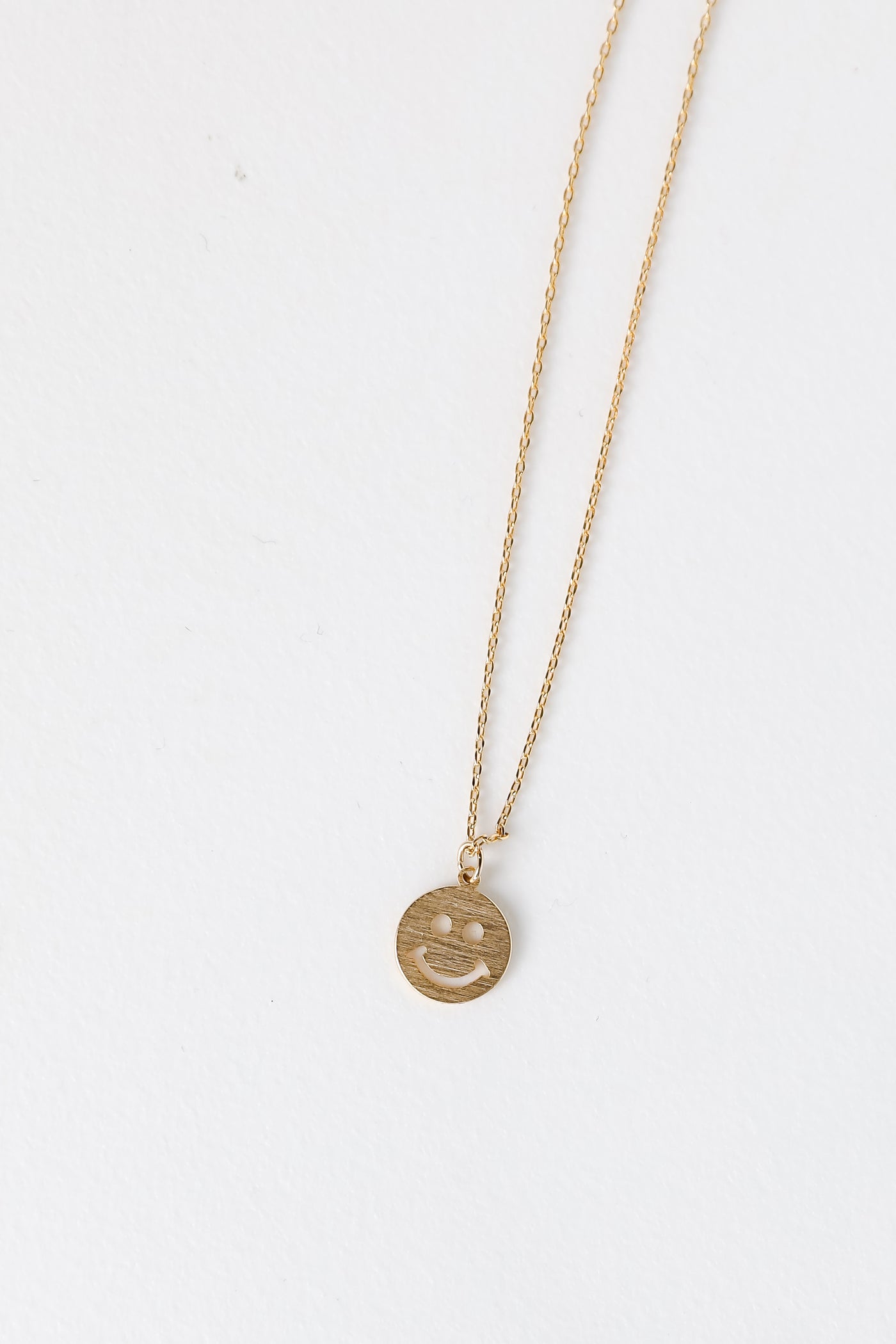 Gold Smiley Face Charm Necklace flat lay